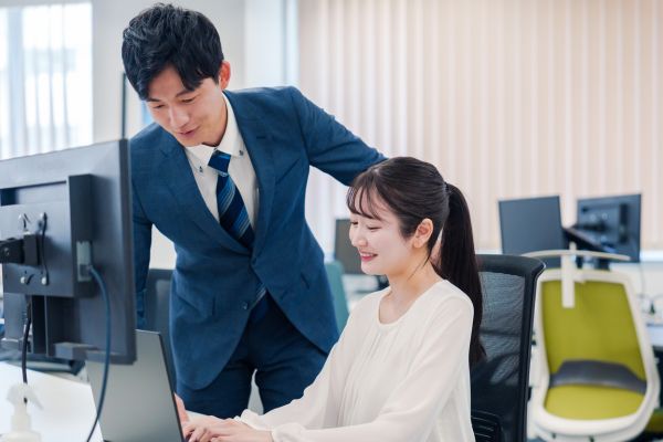Coworkers reviewing work together at a computer in an office.
